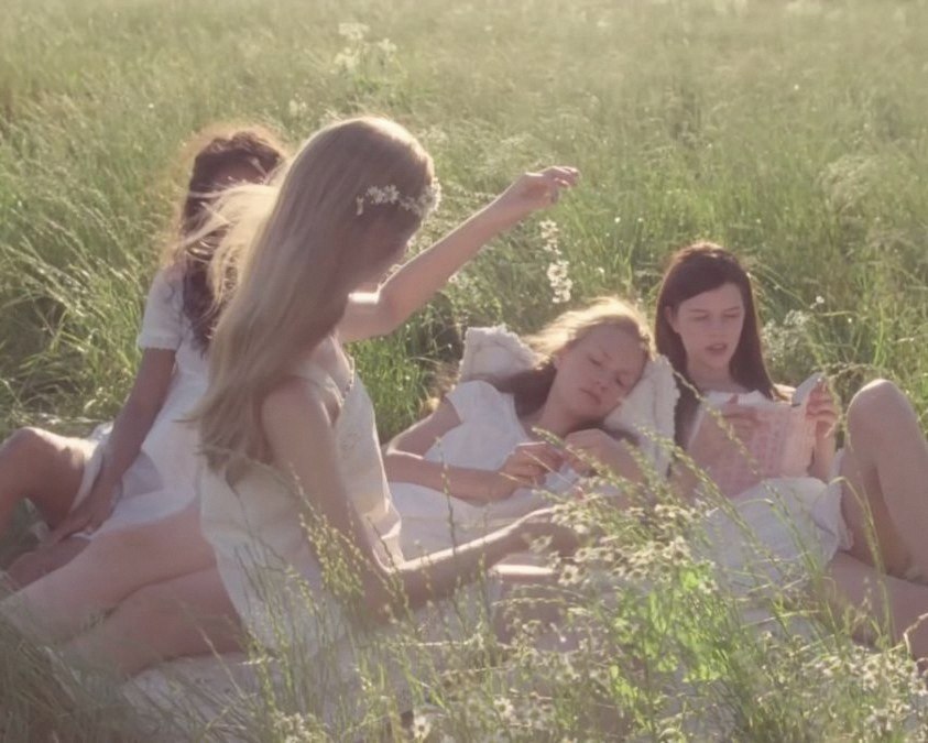 Girls in white dresses lying and reading in tall grass